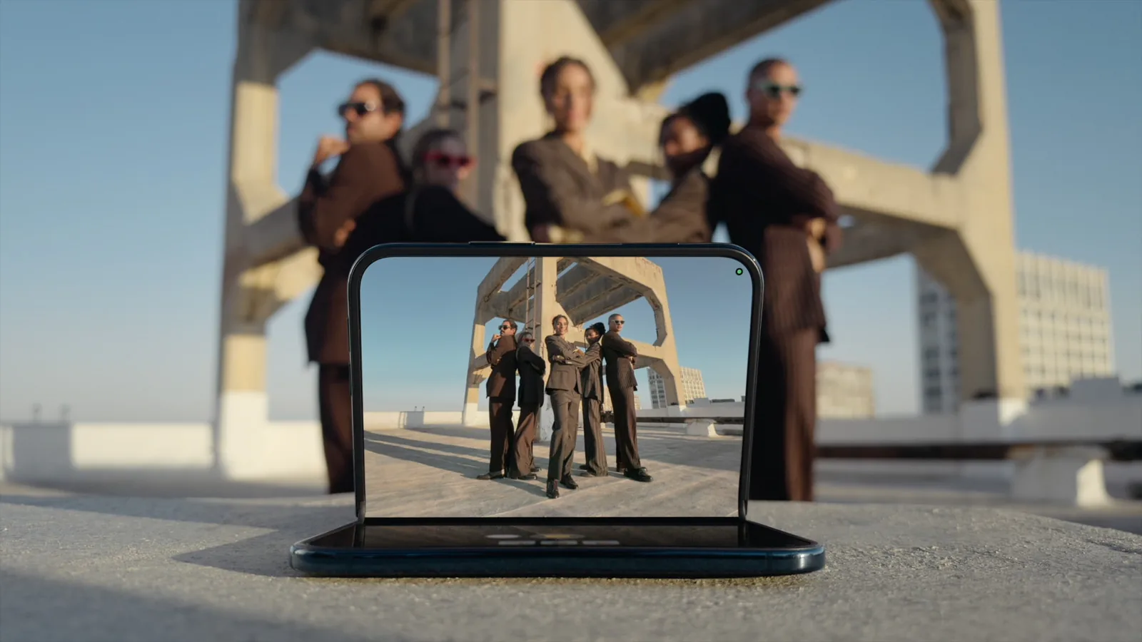 iPhone Duo half folded on a rooftop, the Camera app on the upright half framing five people posing behind it