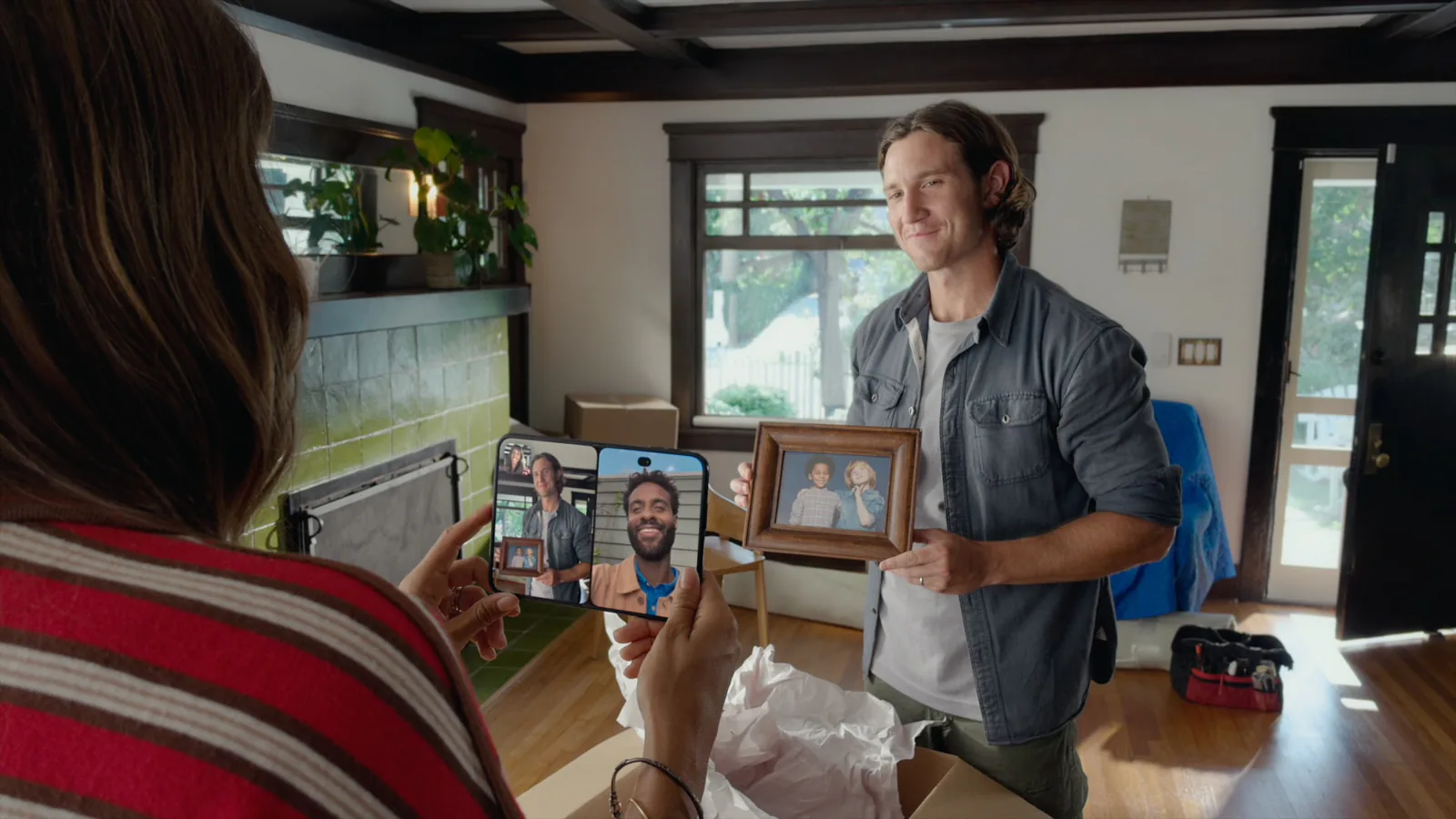 A FaceTime call on the open iPhone Duo held in two hands: the person in the room, filmed by the rear camera, on the left half and the caller on the right