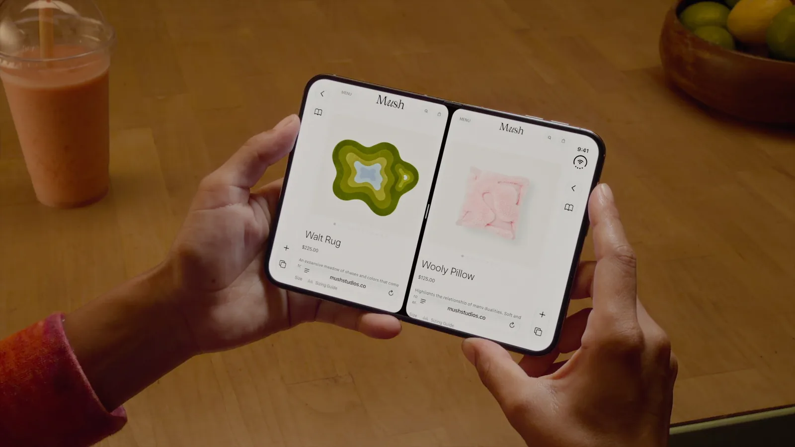 Two hands hold the open iPhone Duo over a table, the same online shop open on both halves in Split View